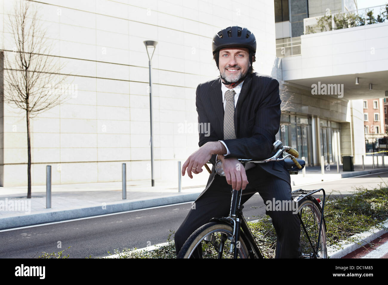 Mid adult businessman sitting on bike, smiling Stock Photo