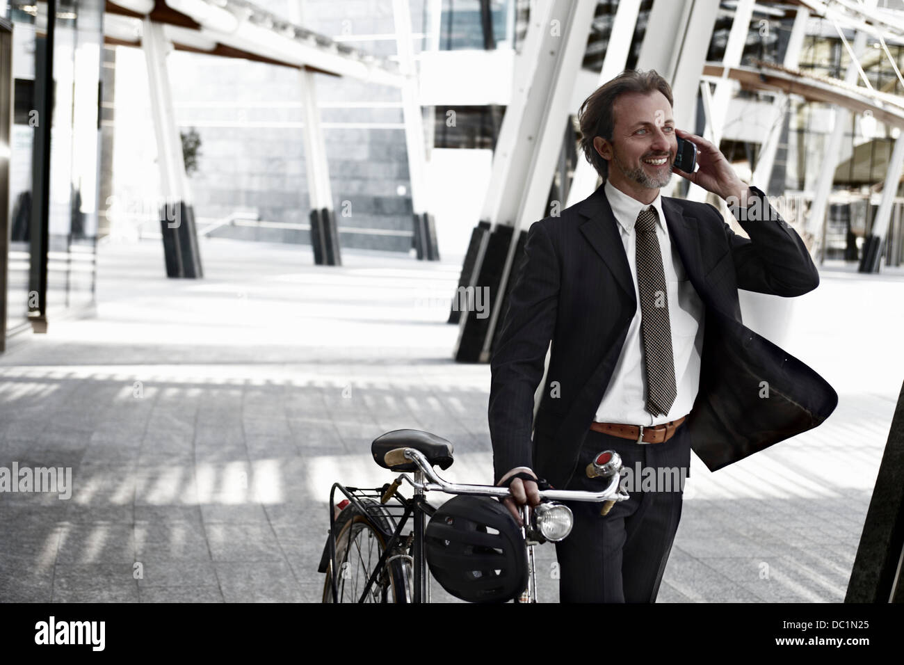 Mid adult businessman walking with bicycle and using mobile phone Stock Photo