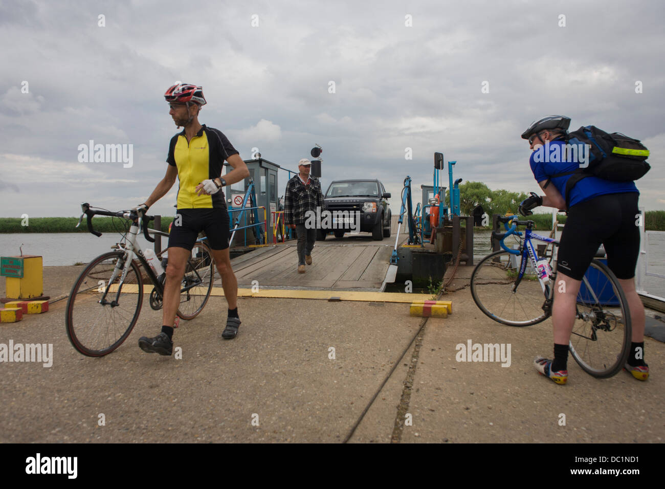 Cyclists disembarking and boarding the small chain ferry crossing the River Yare in Reedham on the Norfolk Broads. Stock Photo