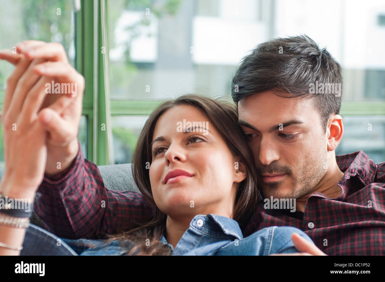Young couple lounging on sofa holding hands Stock Photo