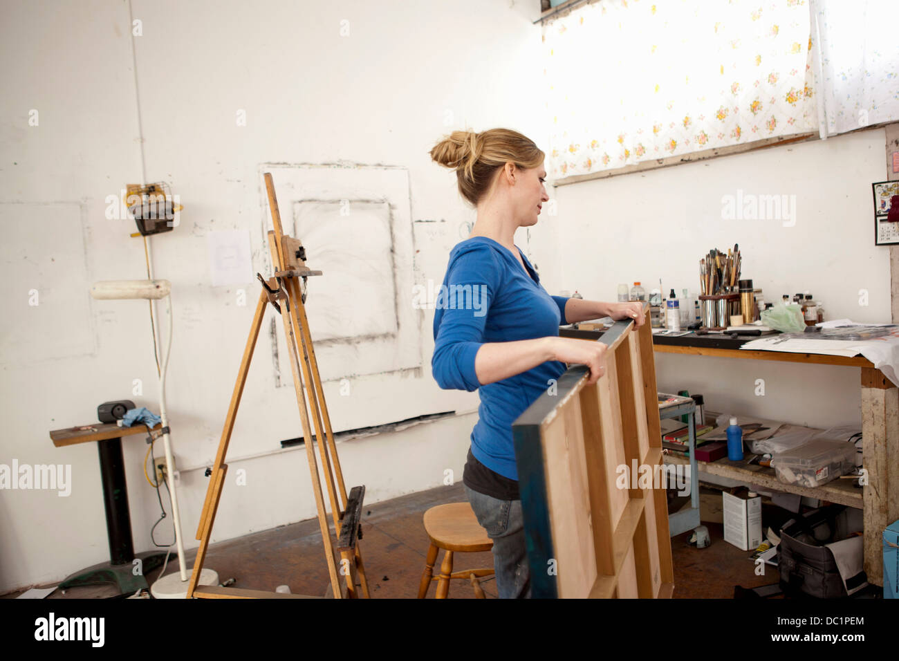 Mid adult woman carrying oil painting in artist's studio Stock Photo