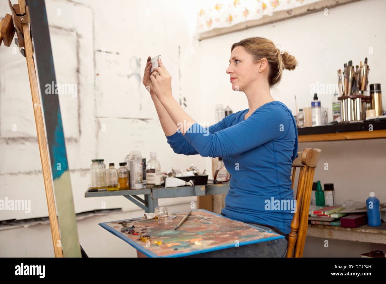 Mid adult woman photographing oil painting in artist's studio Stock Photo