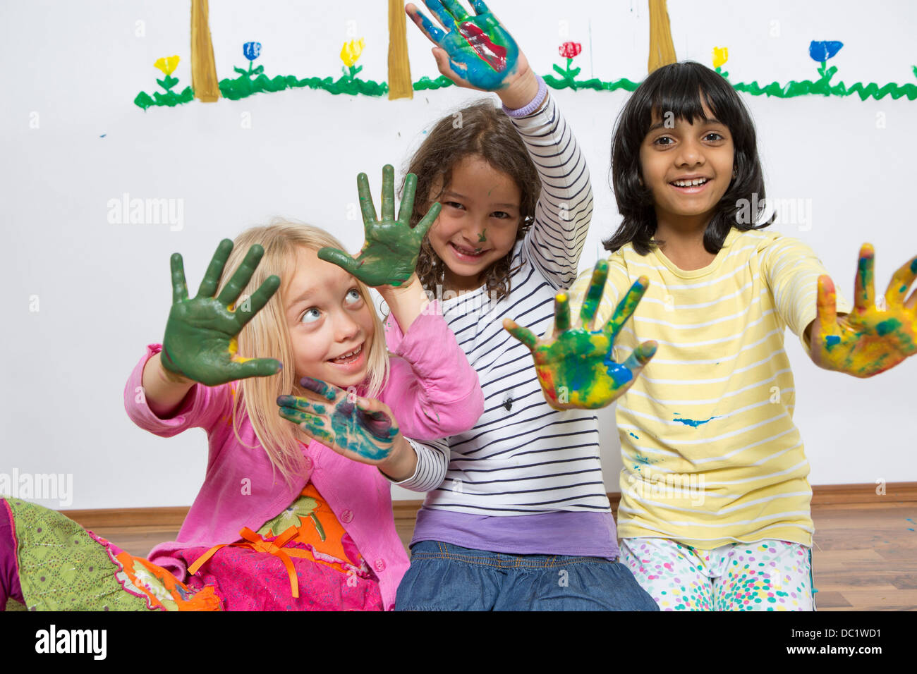 Three girls kneeling on floor with painted hands Stock Photo