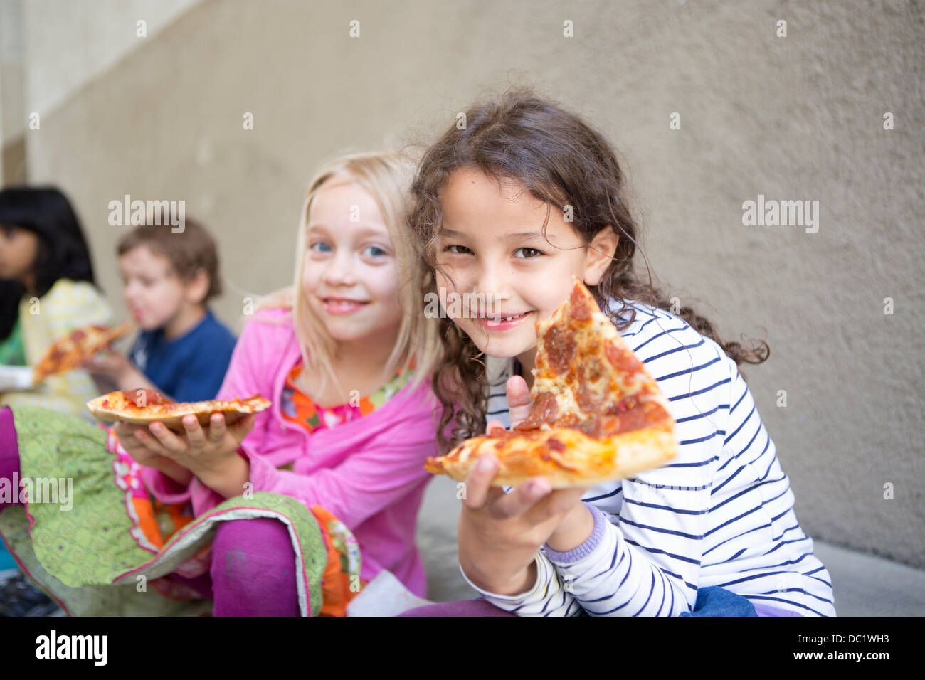 Small group of children eating pizza outdoors Stock Photo