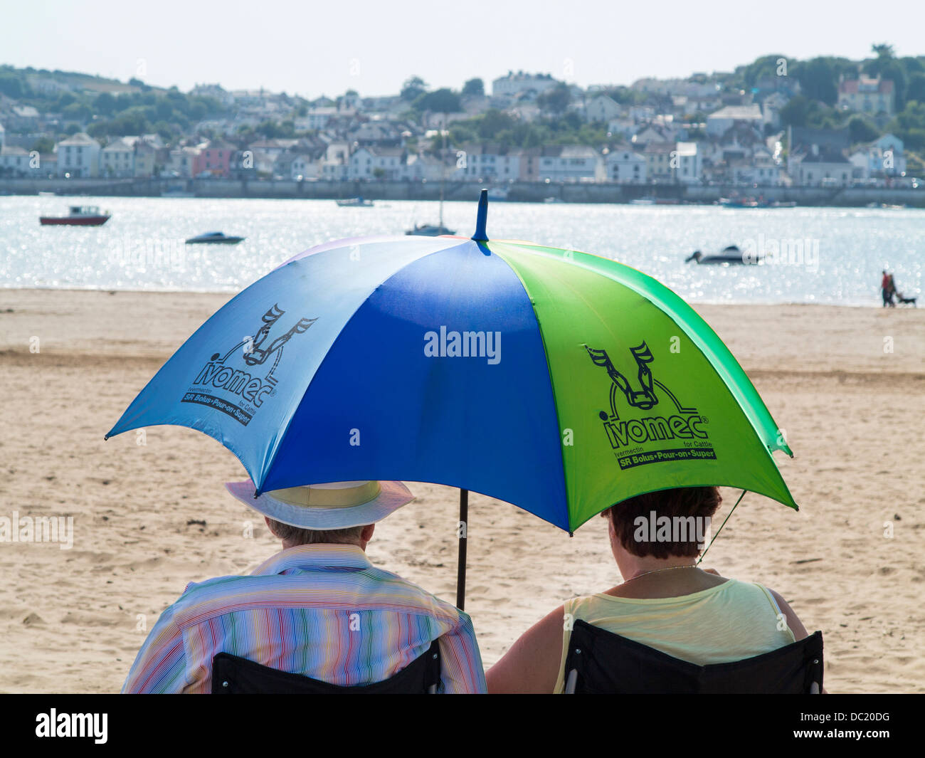 Couple sitting on Instow beach using an umbrella as a parasol, North Devon, England Stock Photo