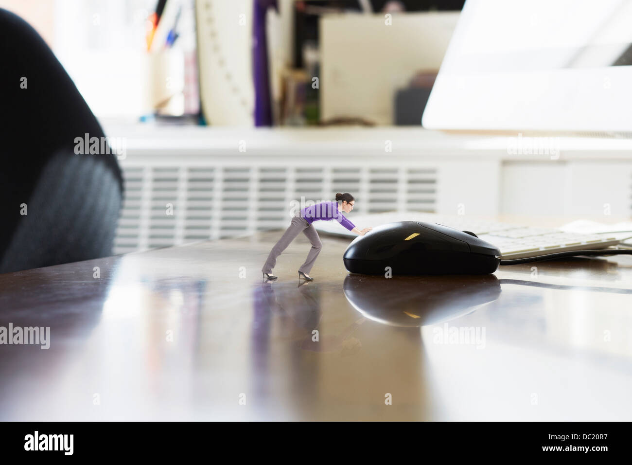 Businesswoman pushing large computer mouse on oversized desk Stock