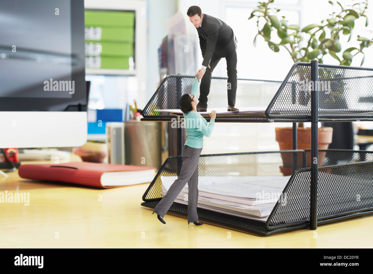 Businessman offering helping hand to colleague on large inbox on oversized desk Stock Photo