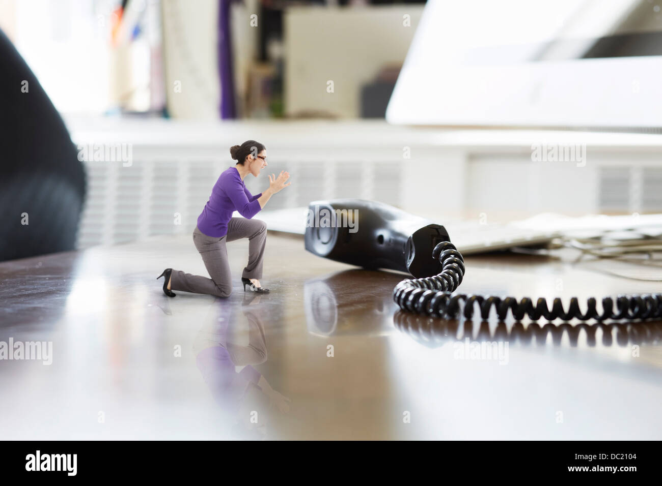 Businesswoman shouting through large telephone receiver on oversized desk Stock Photo