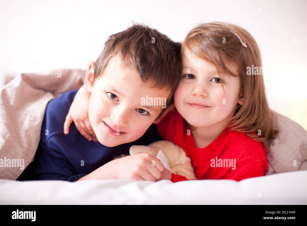 Two young children hugging under duvet Stock Photo Alamy
