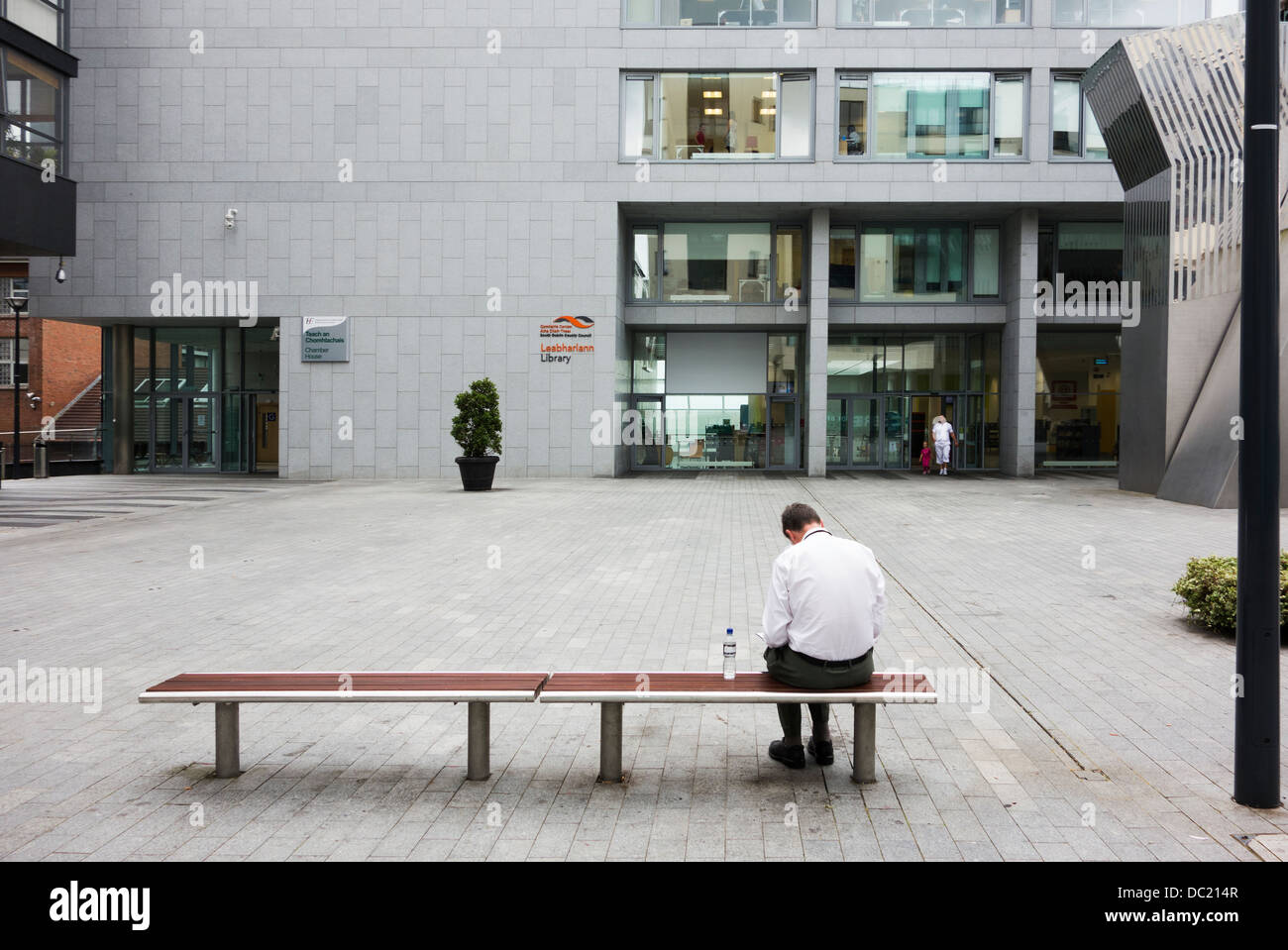 Rear view of man reading while sitting on bench in public square / area - Dublin Ireland Stock Photo