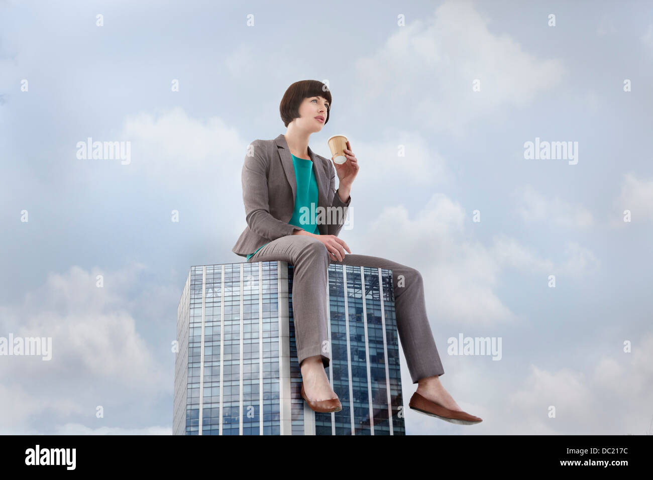 Oversized businesswoman sitting on skyscraper, low angle view Stock Photo