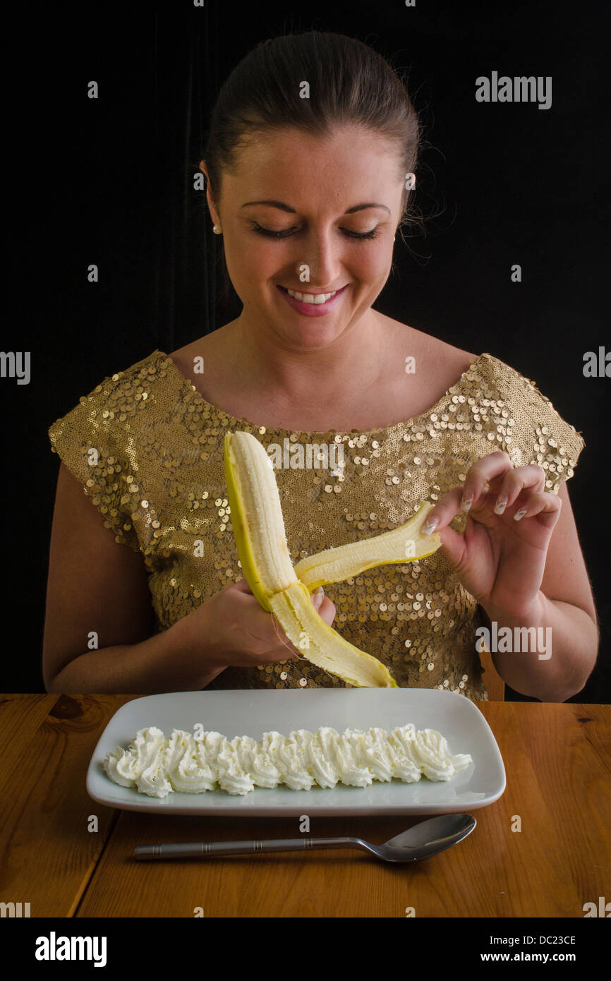 Smiling young woman peeling a banana with squirty cream on a plate Stock  Photo - Alamy