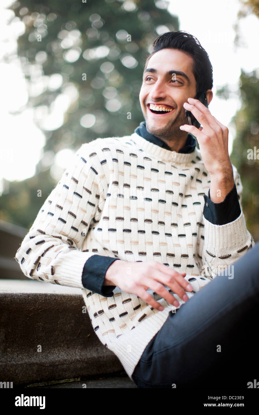 Young man sitting and using mobile phone, smiling Stock Photo