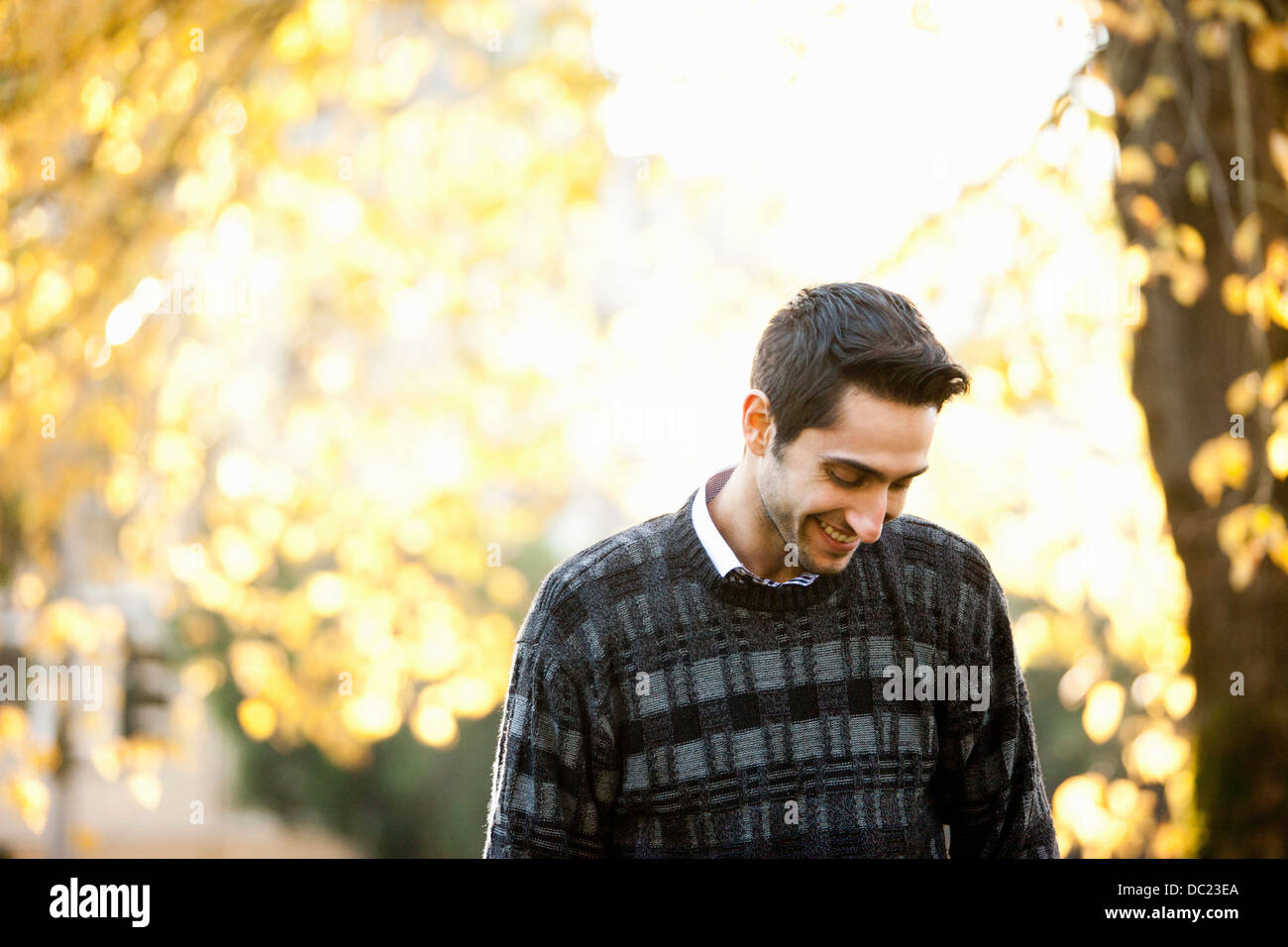 Young man looking down in sunlit park, smiling Stock Photo