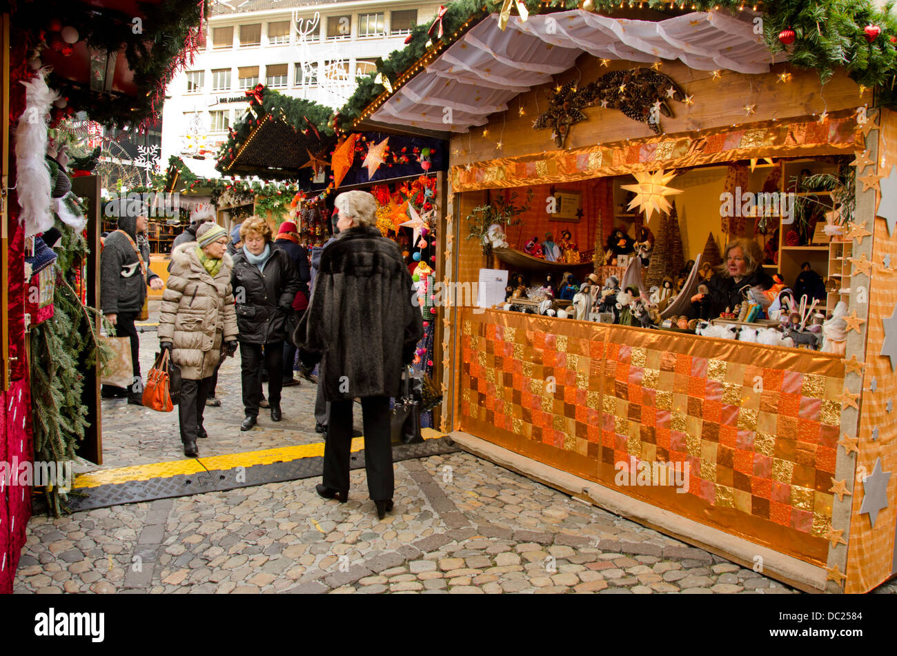 Switzerland, Basel. Basel Winter Holiday Market at Barfusserplatz. Typical vendor stand at winter market with people shopping. Stock Photo