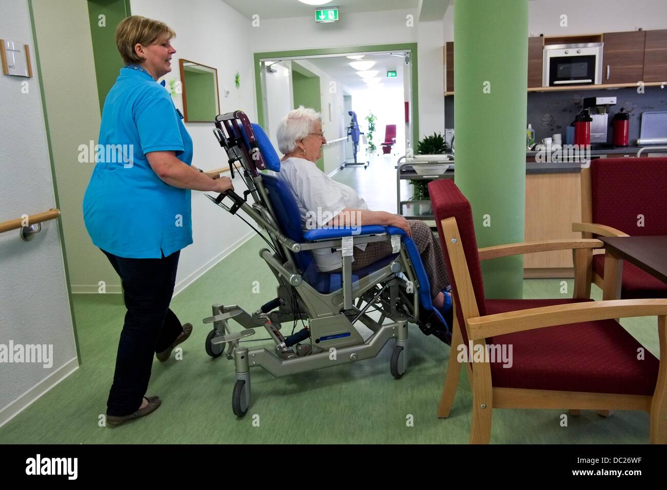 Nurse Anja von Westerhagen pushes resident of the nursing home Heidemarie Mueller-Hein along a hallway of the care home APE with a wheelchair in Hanover, Germany, 11 June 2013. As of recently, the city of Hanover has a nursing home for people who are overweight. Photo: Peter Steffen Stock Photo