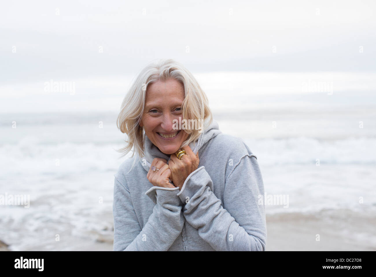 Mature woman wearing grey sweater on beach, smiling Stock Photo