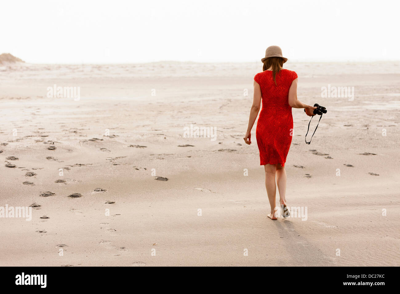 Mature woman wearing red dress walking on beach Stock Photo