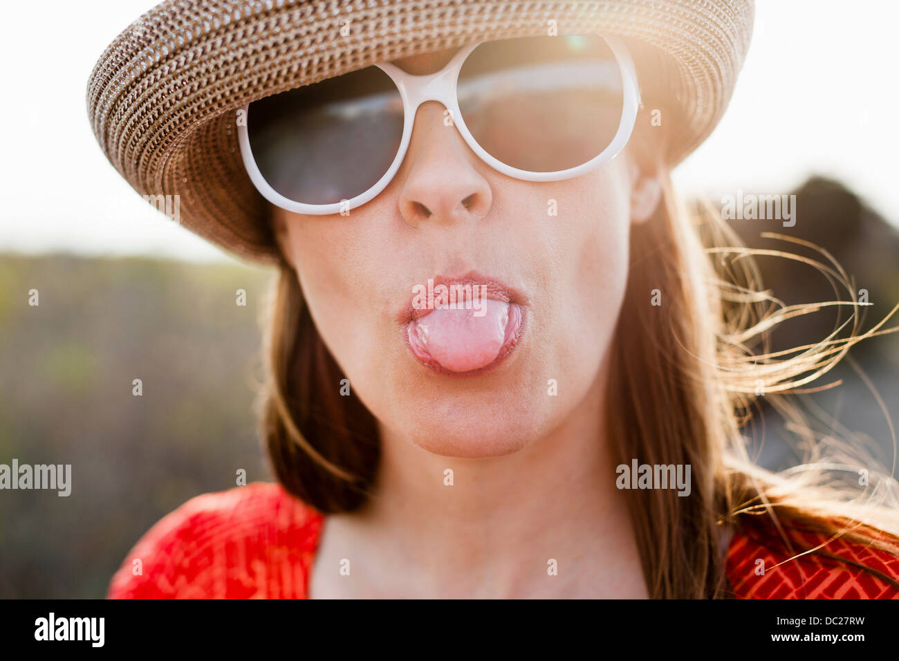 Mature woman wearing sunglasses and sunhat sticking out tongue Stock Photo