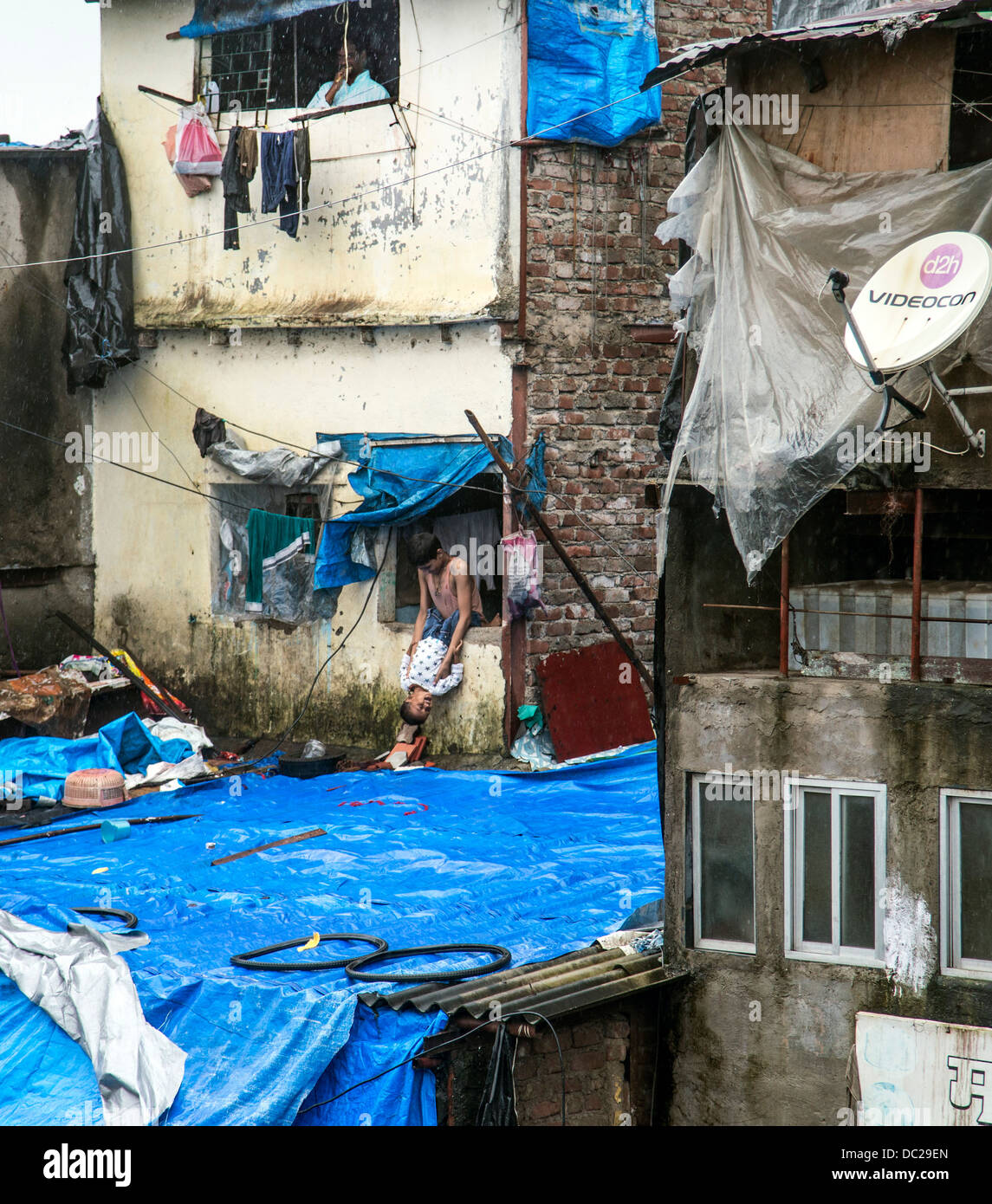 Slum buildings life children playing hanging out of window held by legs whilst father brushes teeth upstairs Stock Photo