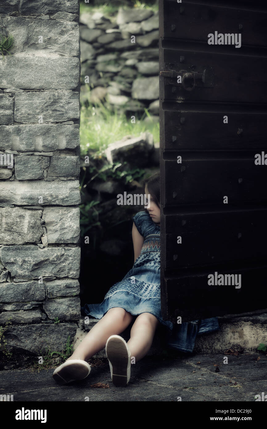 a sad, young girl is sitting in an old door Stock Photo