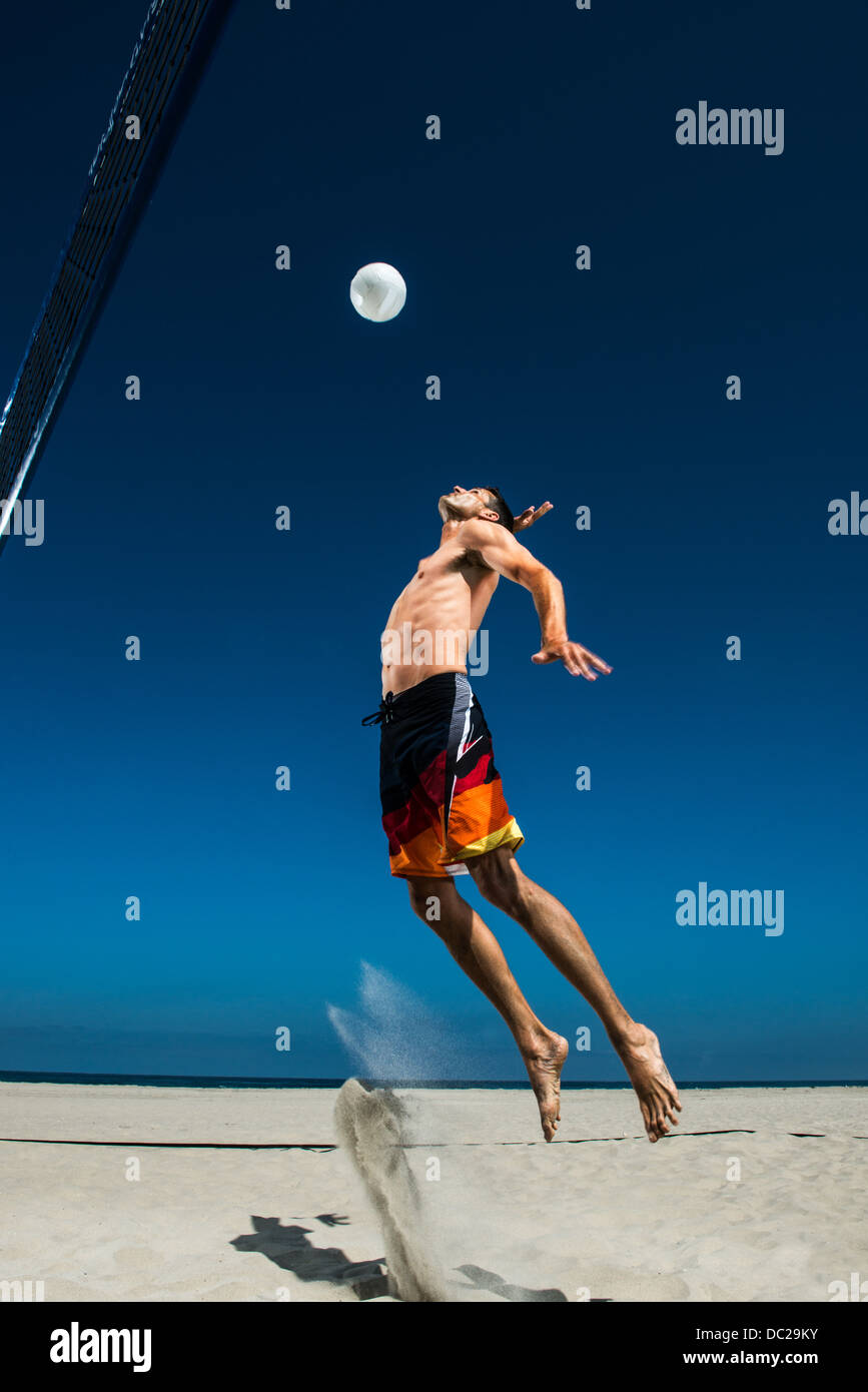 Male beach volleyball player jumping mid air to hit ball Stock Photo