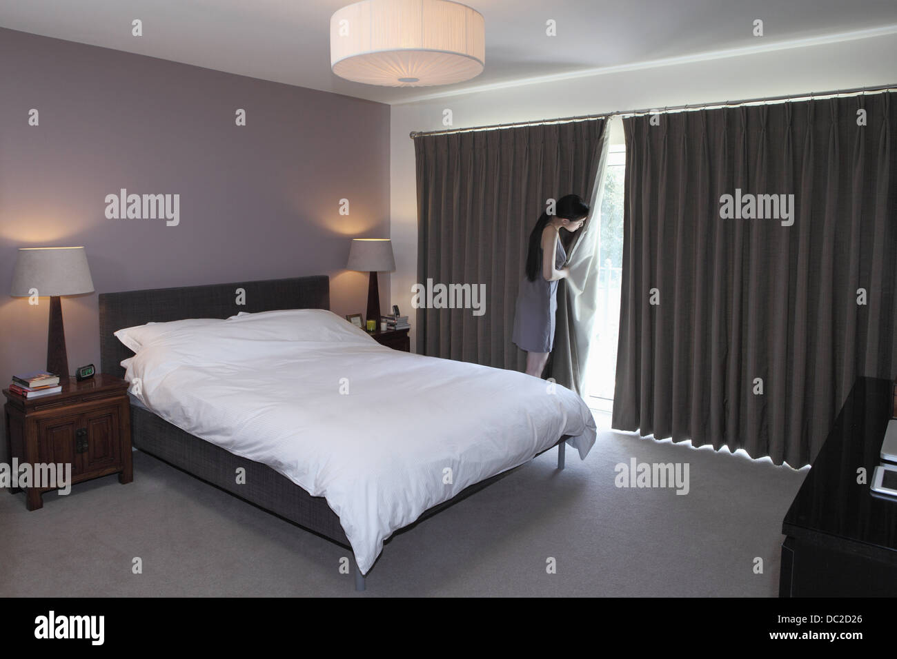 Woman peeping behind bedroom curtain Stock Photo