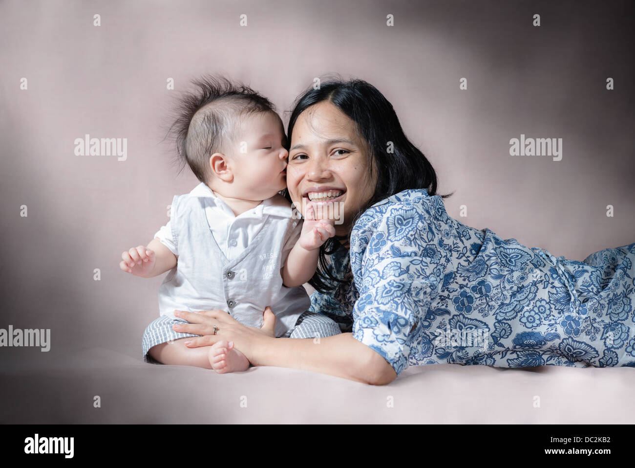 One image from a series of 3 photos of a gorgeous 5 month old mixed race Asian Caucasian baby sitting and kissing his mother Stock Photo