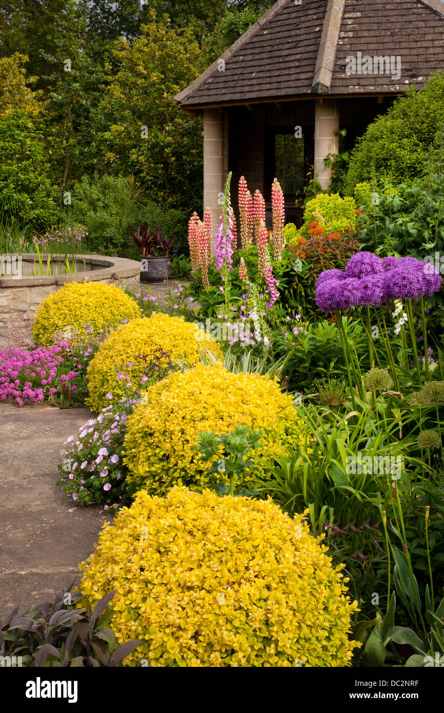 Summer flower boarder with purple Allium, delphiniums and foxgloves with stone summerhouse in English garden, England Stock Photo