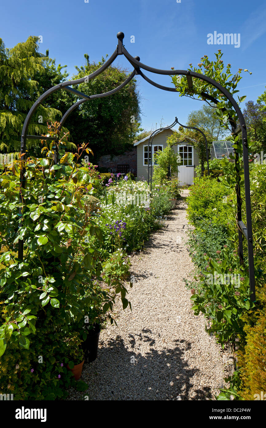 Metal arch leading on a gravel path to flower boarder and summerhouse on English garden, England Stock Photo