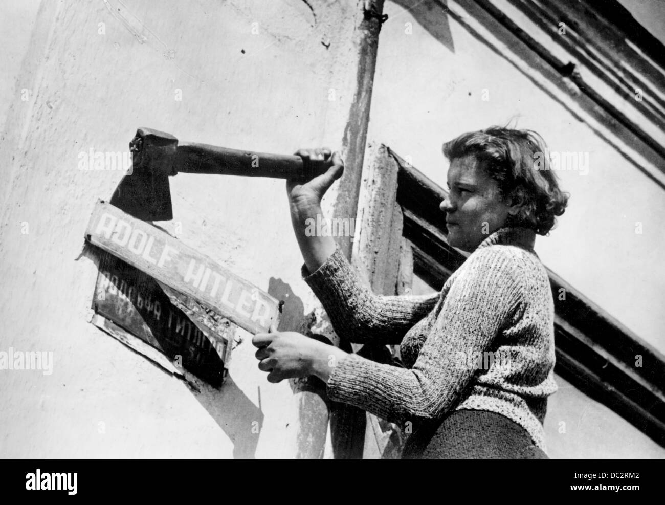 A woman removes the street sign of a street renamed 'Adolf Hitler', revealing the original street sign with Russian letters, at the end of World War II. Date and place unknown. Fotoarchiv für Zeitgeschichte Stock Photo