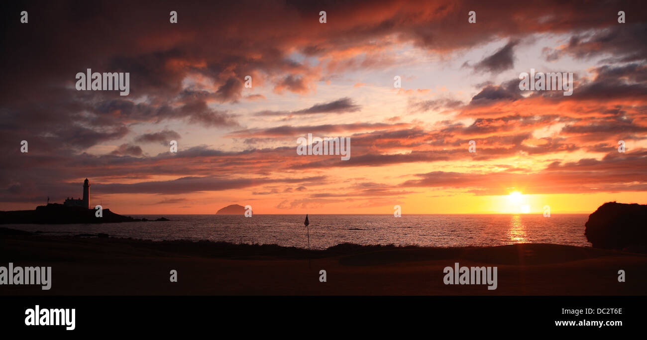 Sunset over Ailsa Craig with lighthouse, orange sky and clouds and golf flag. Stock Photo