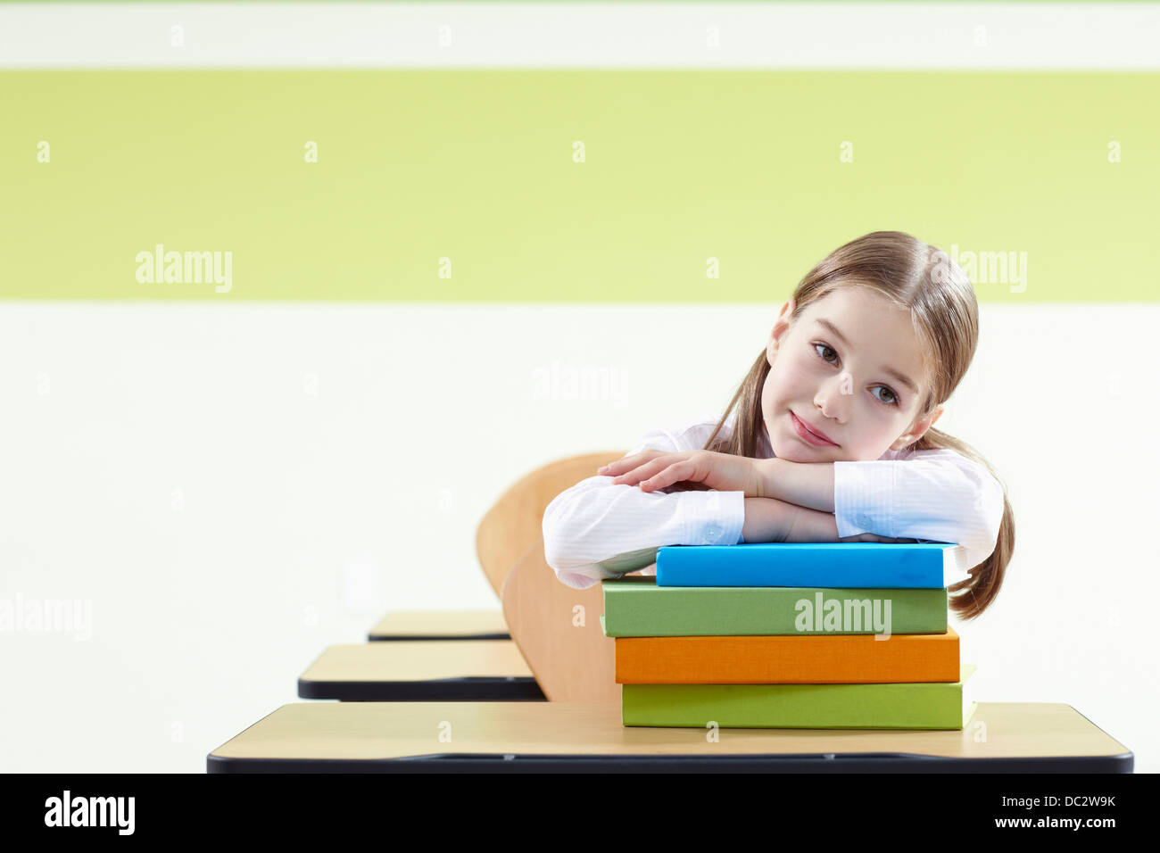 a girl leaning on a pile of books in a classroom Stock Photo - Alamy