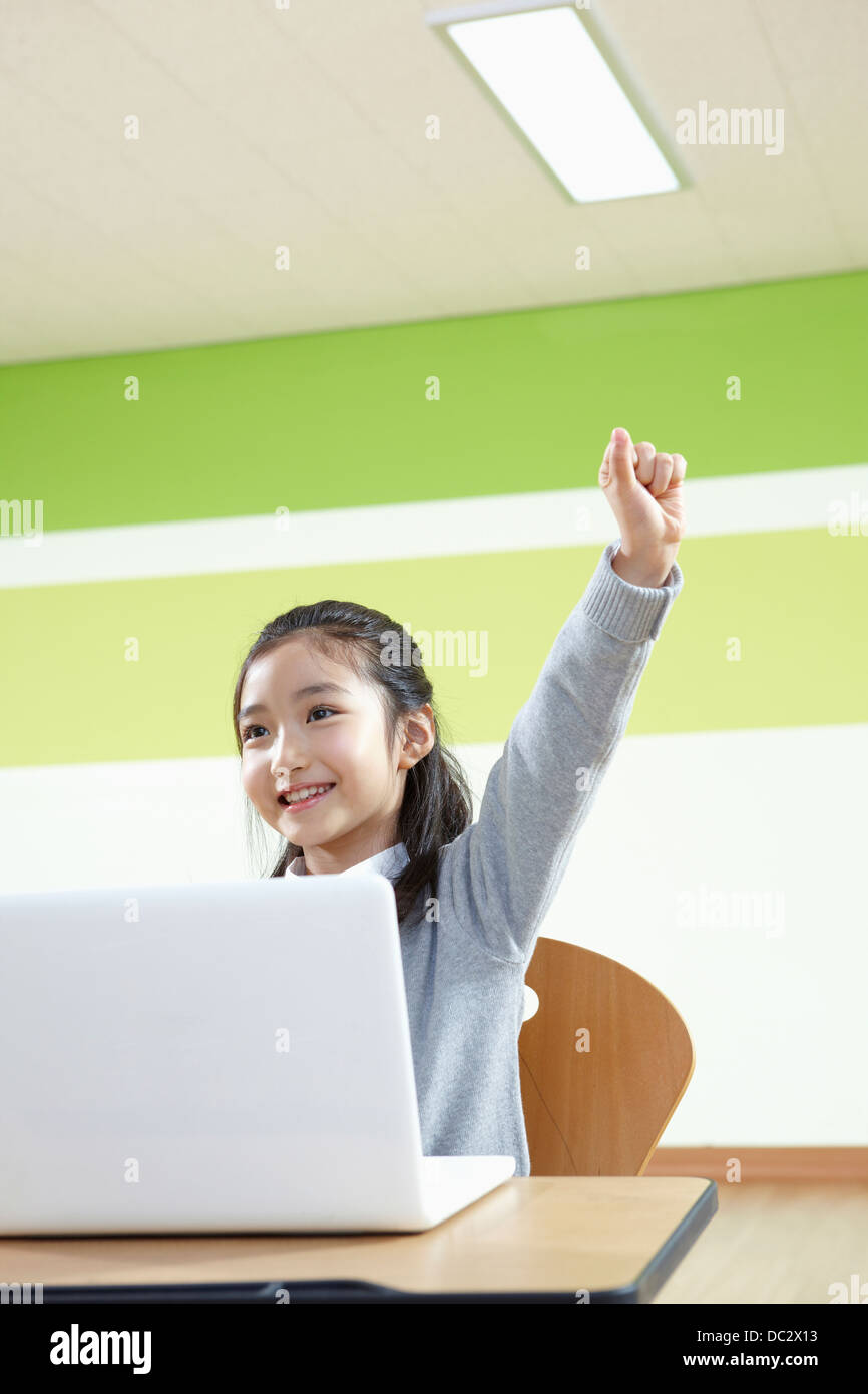a girl raising her hand while using a laptop in a classroom Stock Photo ...