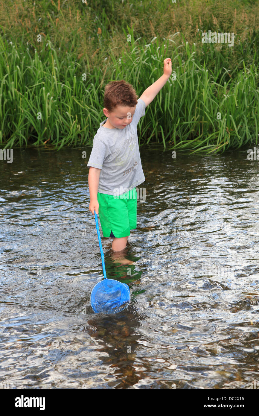 Young boy wading in a river trying to catch fish with a fishing net, UK