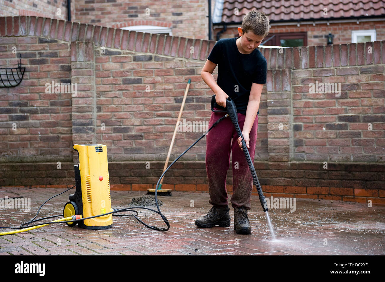 A boy aged 13 uses a power washer to clean the family block pave drive at his home for pocket money. Stock Photo