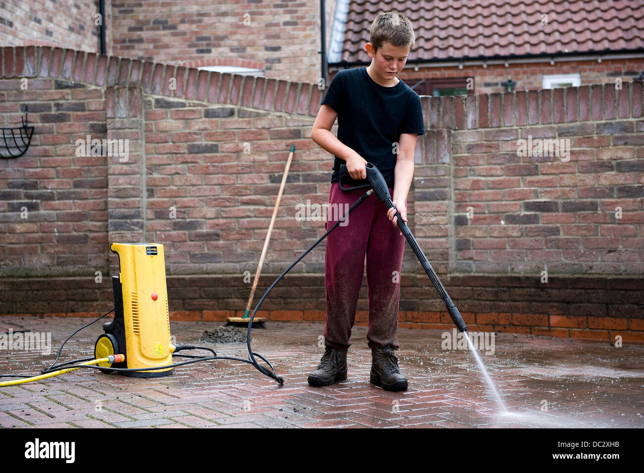 A boy aged 13 uses a power washer to clean the family block pave drive at his home for pocket money. Stock Photo