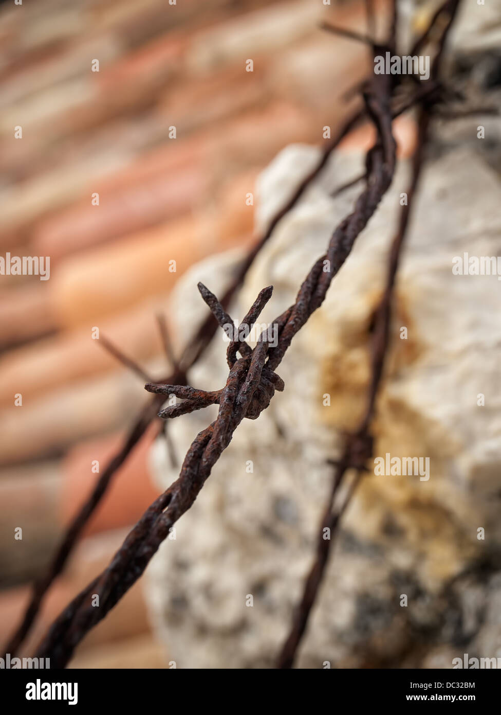 Rusty barbed wire above roof and stone wall. Stock Photo