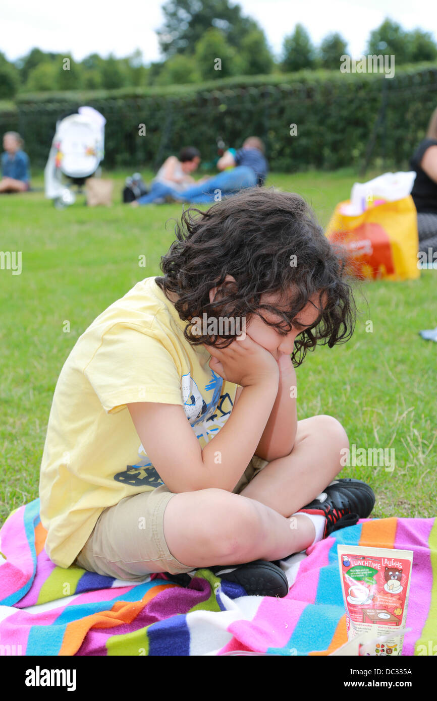 Young boy sitting in the park cross-legged upset. Stock Photo