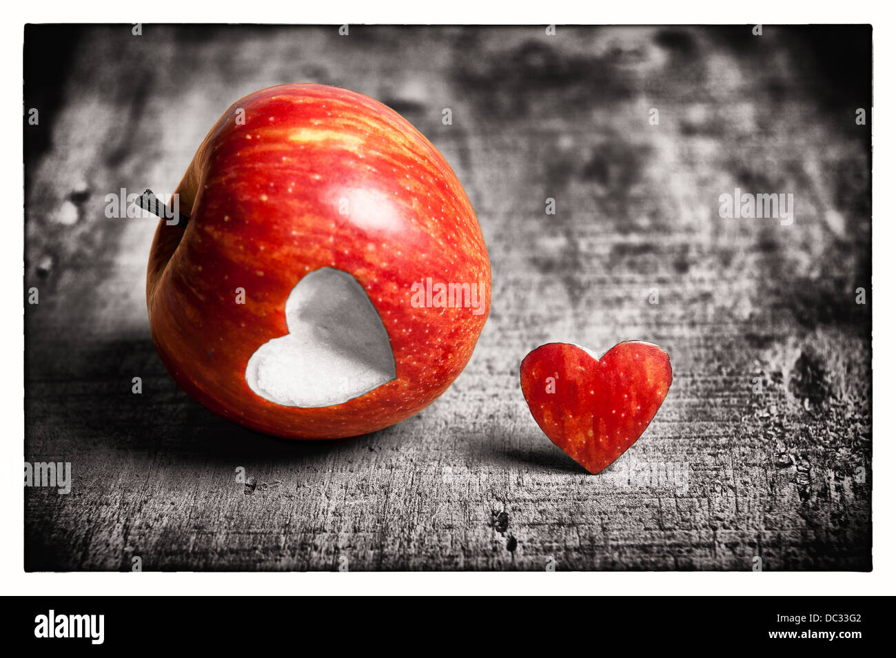 A red apple with a heart shape cut-out. One part is in color and the other part is Black & White. Representation of love. Stock Photo