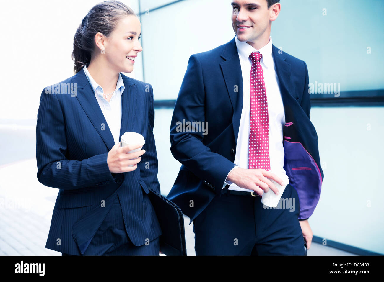 Smiling businessman and businesswoman walking with coffee Stock Photo