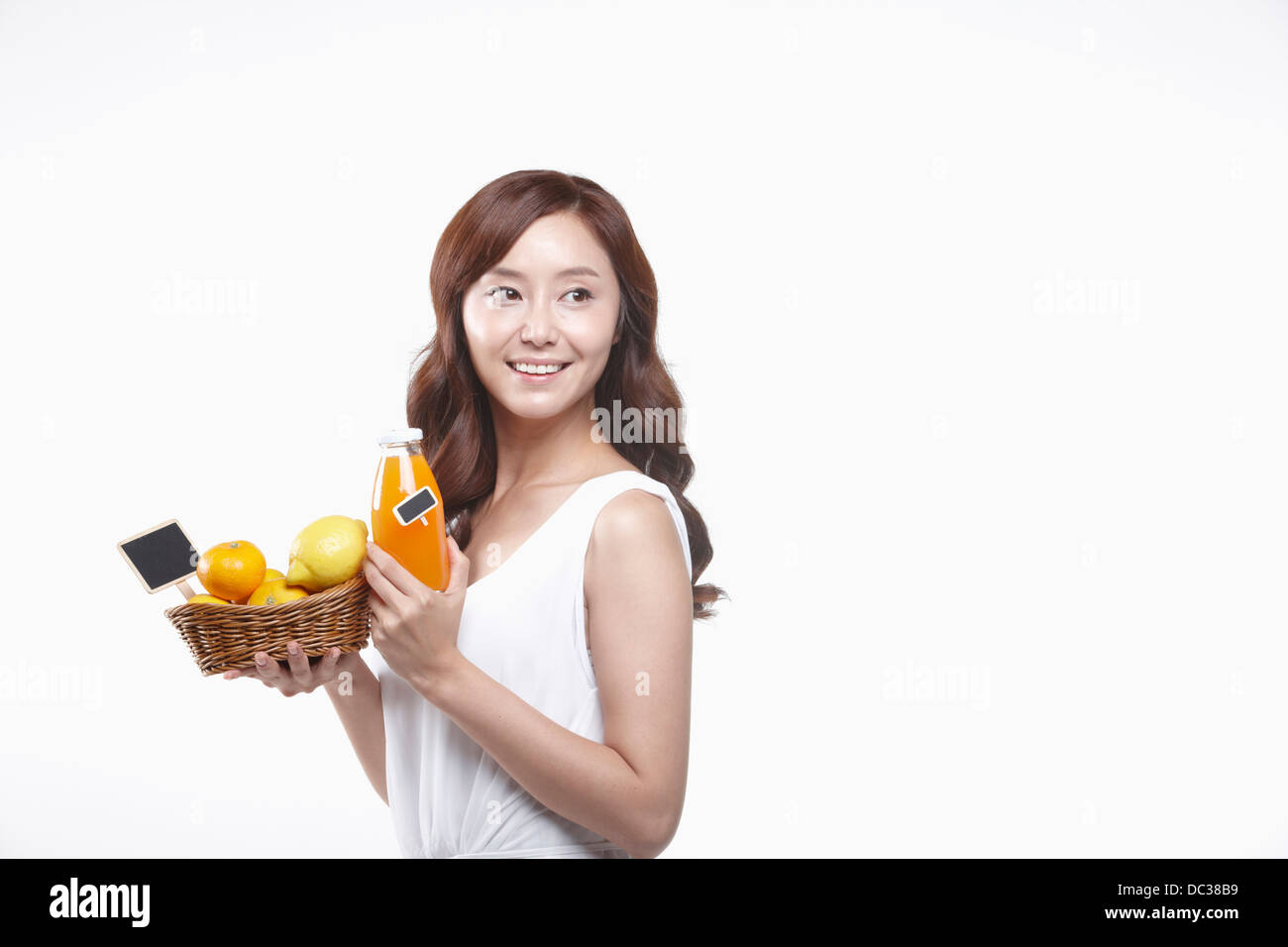 a lady in white dress holding a basket of fruits and a bottle of juice Stock Photo