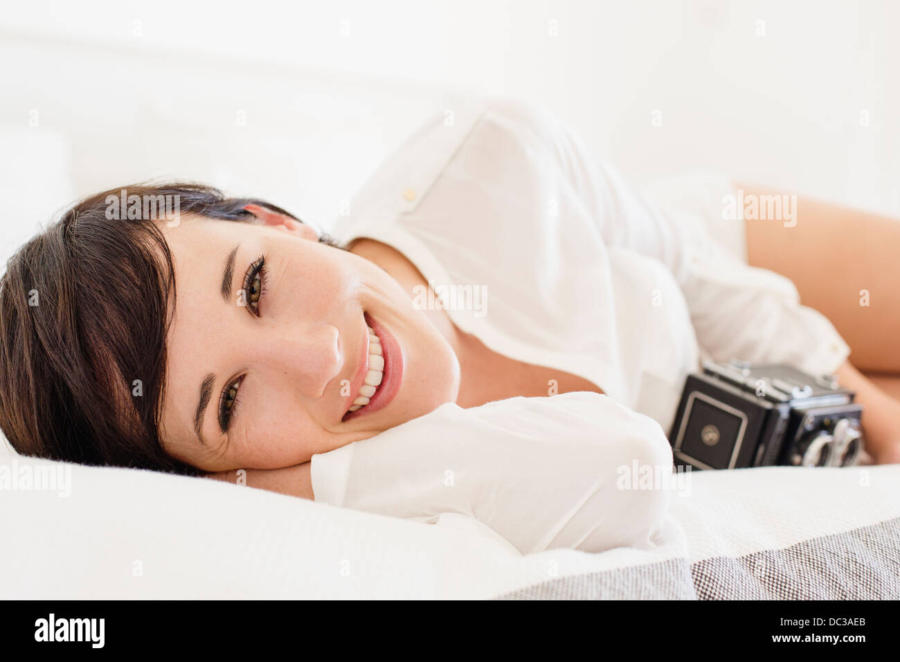 Portrait of smiling woman with vintage camera in bed Stock Photo