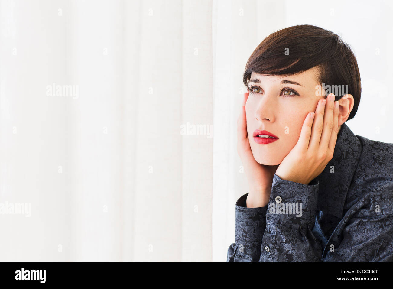 Pensive woman with head in hands looking out window Stock Photo