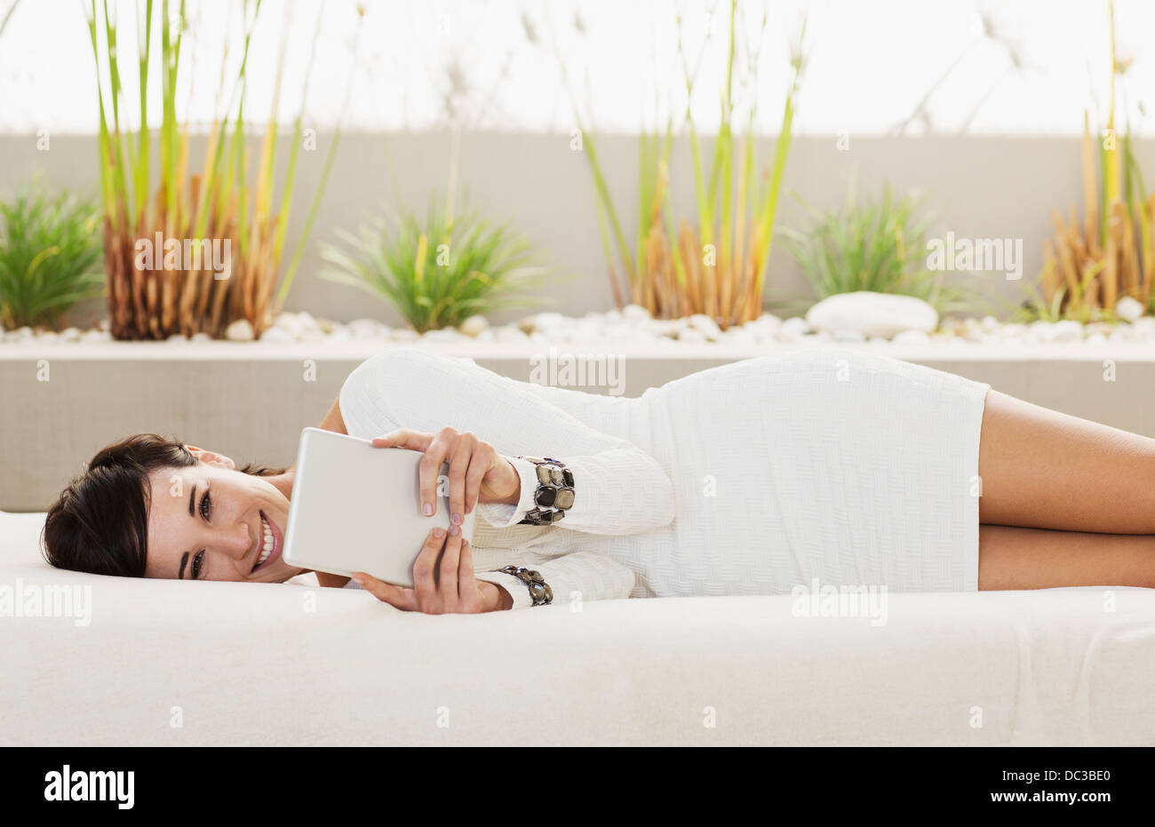 Portrait of smiling woman laying on patio sofa using digital tablet Stock Photo