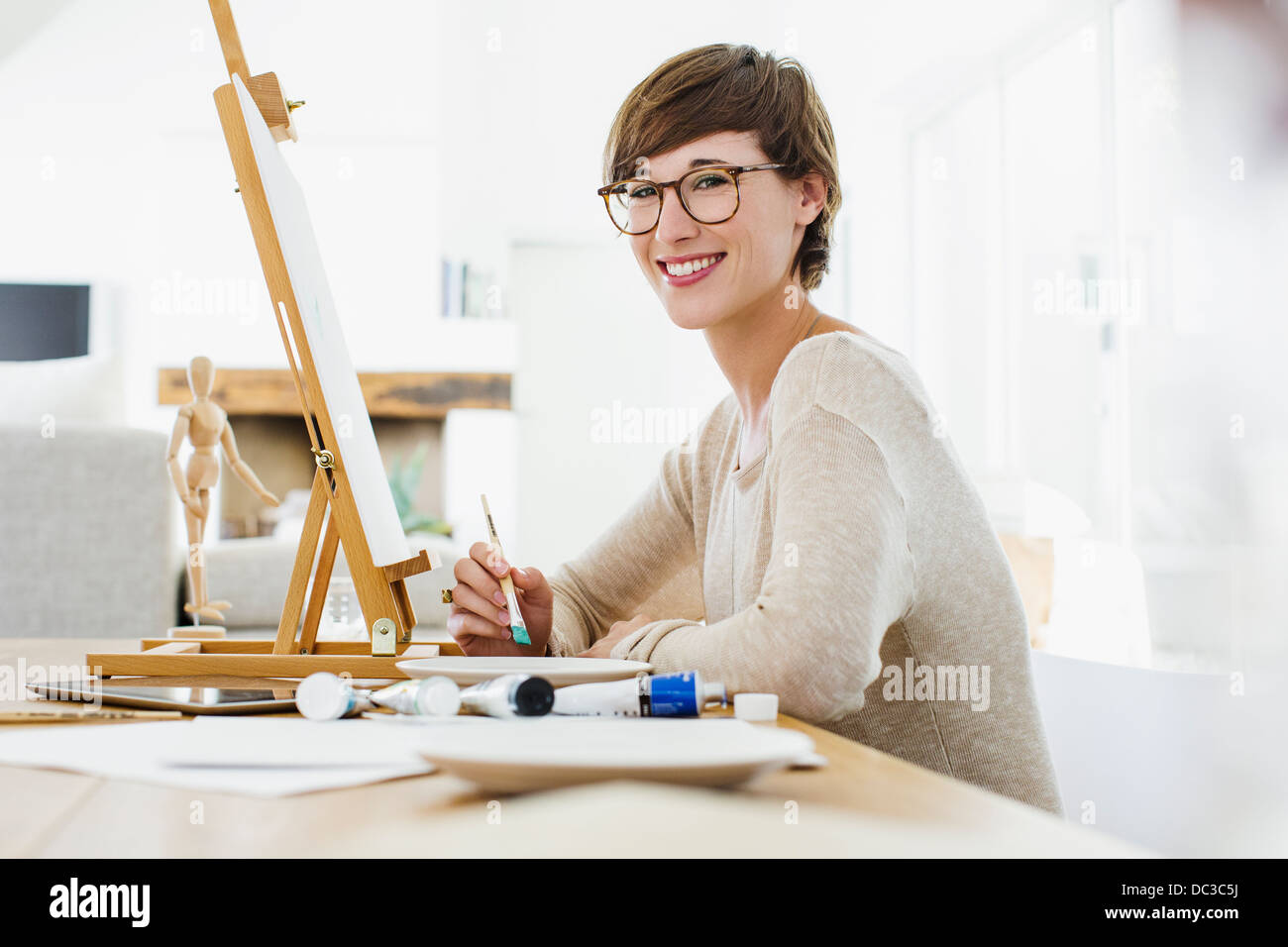 Portrait of smiling woman painting at easel on table Stock Photo