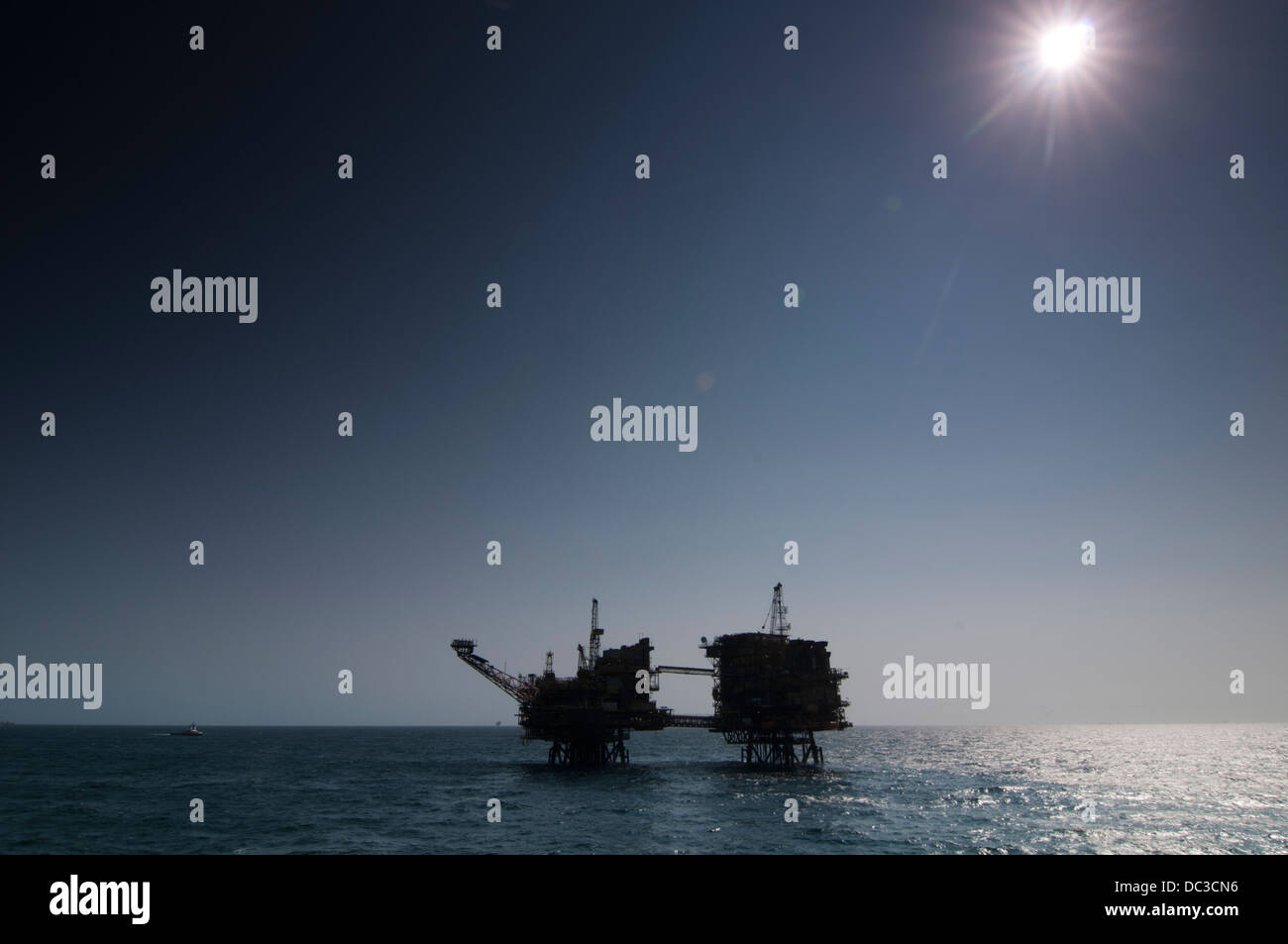 silhouette of an oil rig in offshore area, Hard back light, blue sky, refelection on water surface. Stock Photo