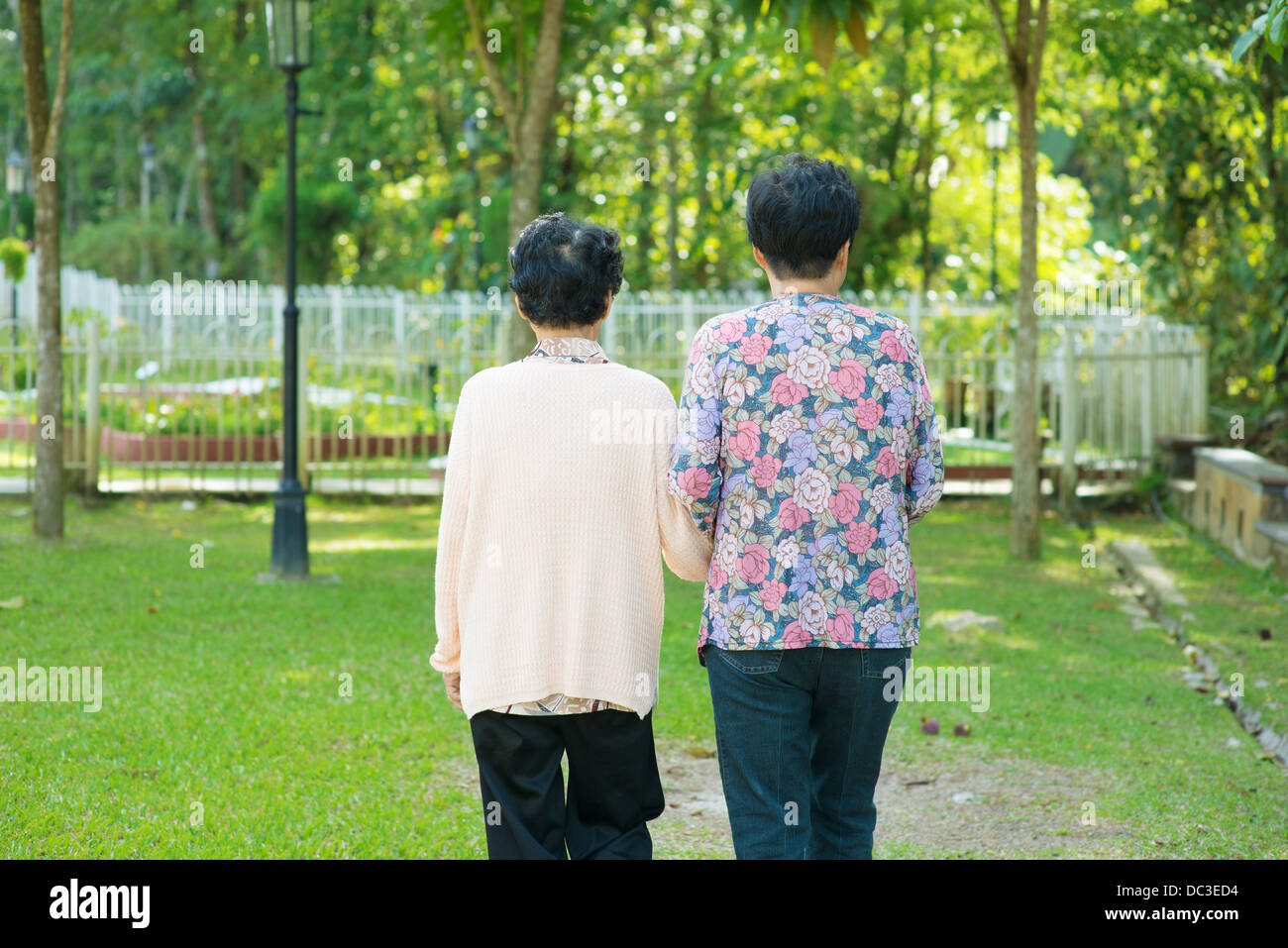 Rear view of Asian 80s old mother and 60s senior daughter holding hands walking at outdoor park. Stock Photo