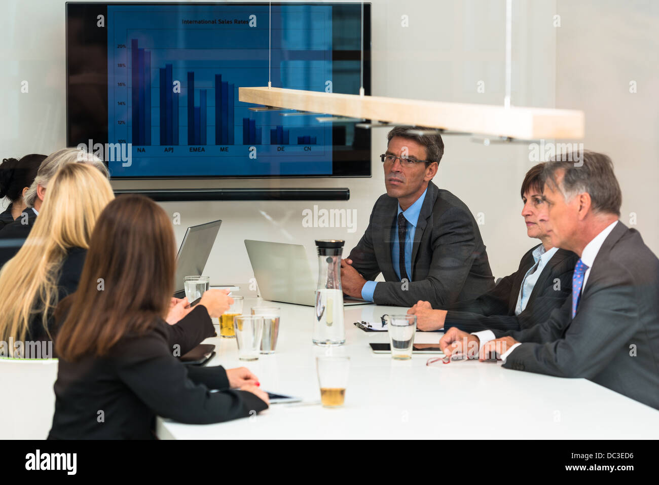 Mixed group in business meeting with laptops, projection screen, digital tablets and smartphones seen through a glass door Stock Photo