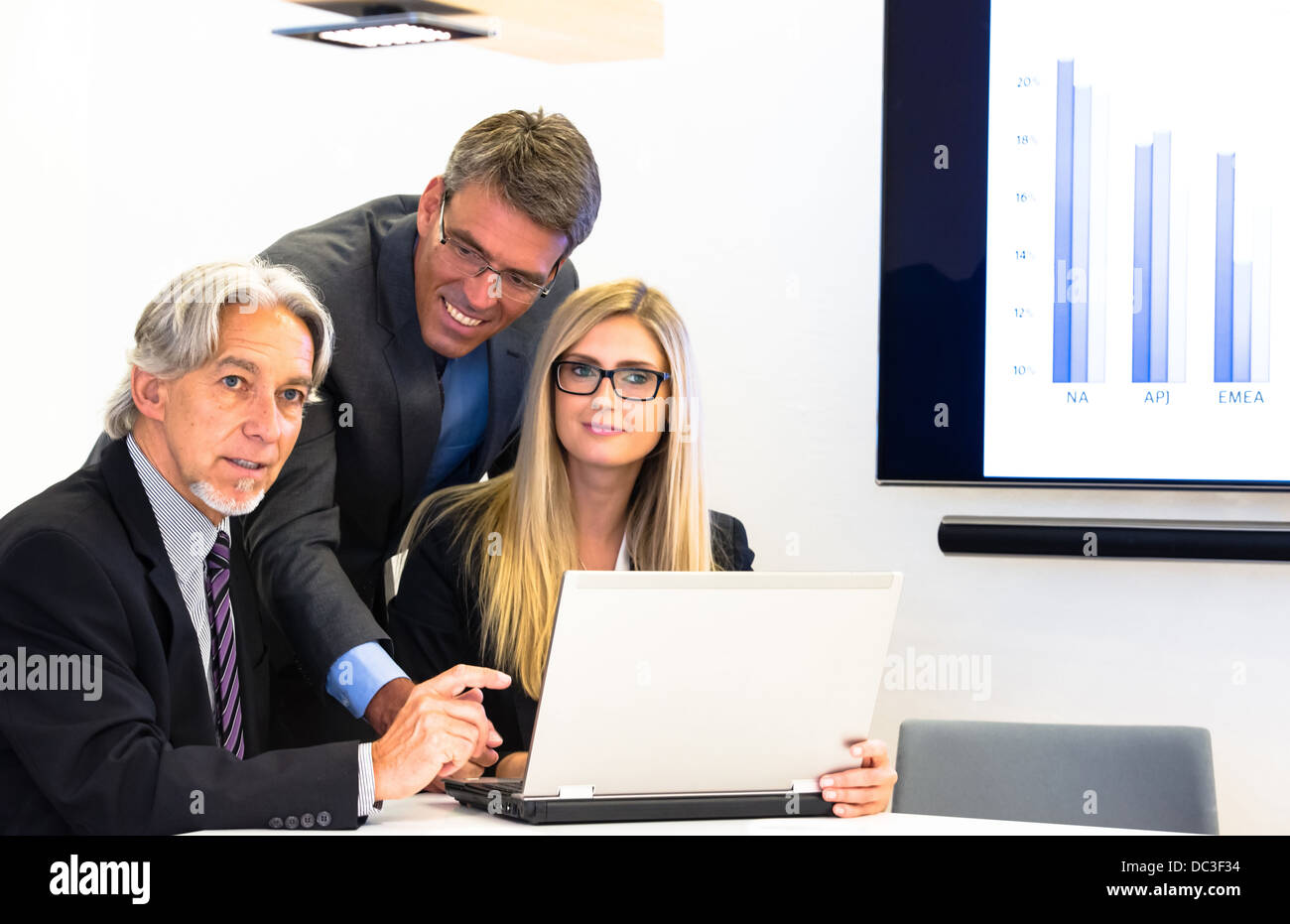 Mixed group in business meeting discussing over the laptop with projection screen, showing the latest sales figures Stock Photo